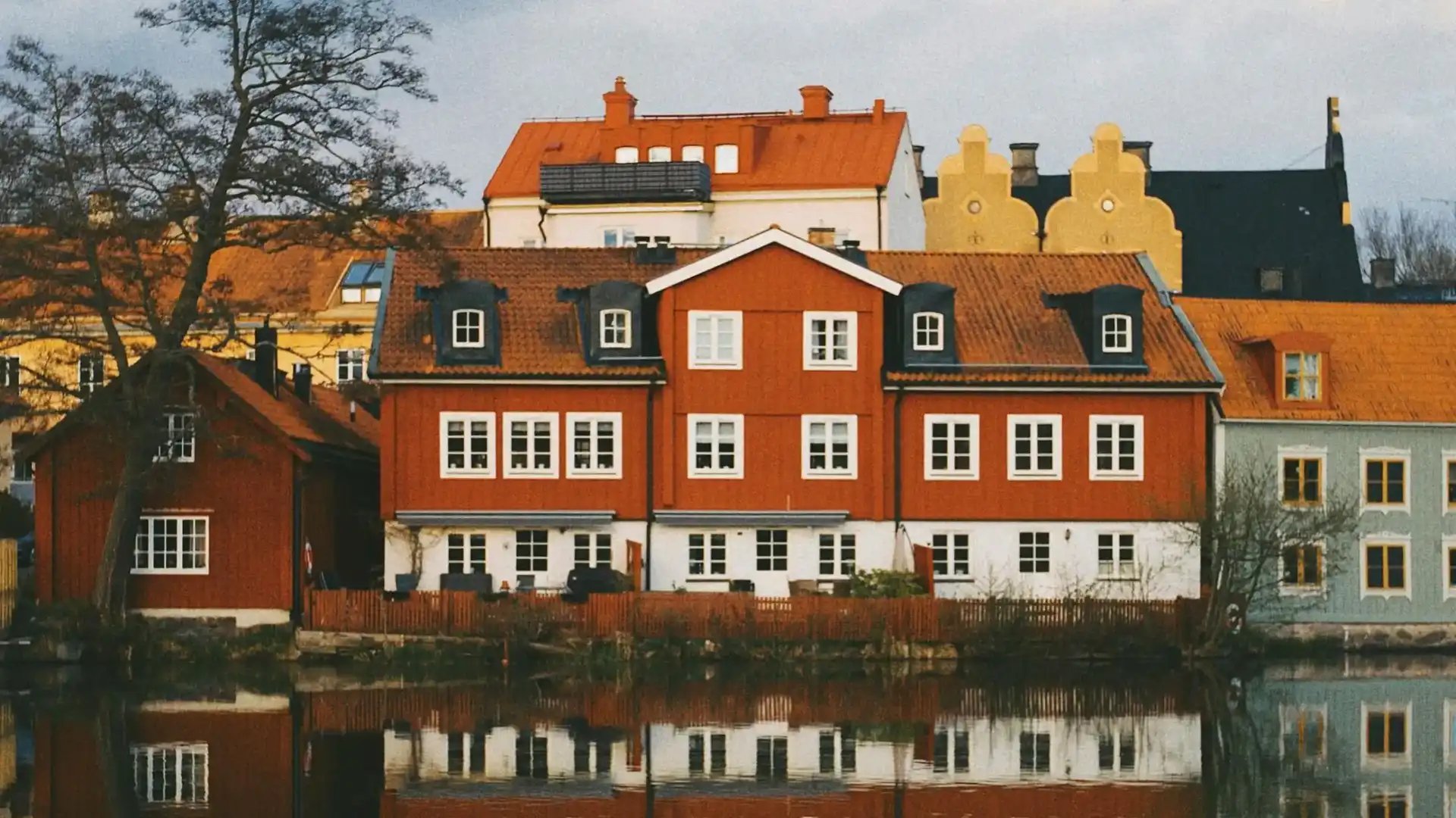 Röda trähus med vita fönster speglas i vattnet.
