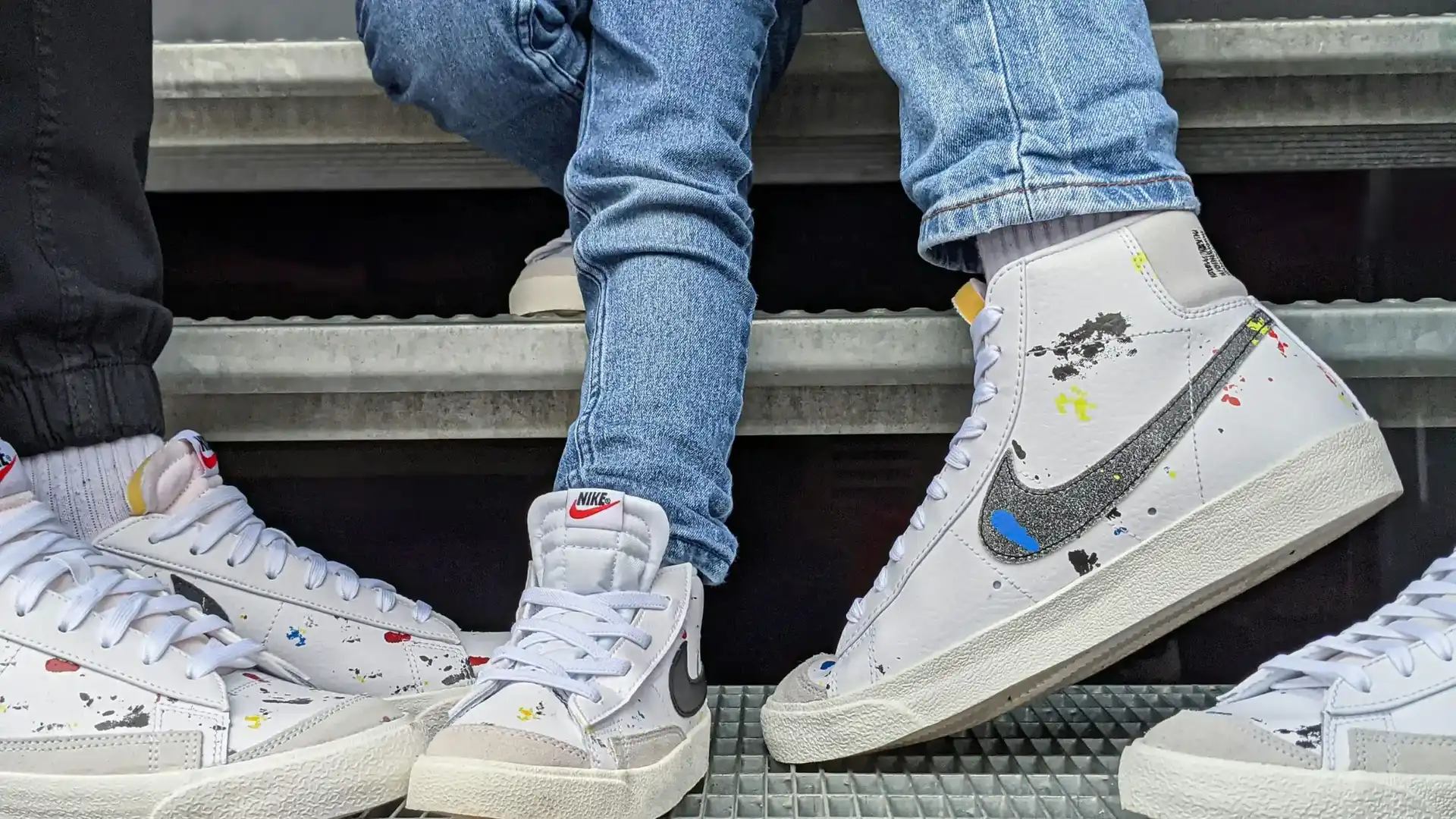 Två personer i jeans bär vita sneakers med färgstänk och Nike-logga.